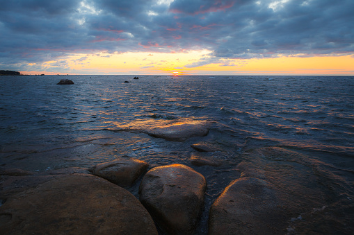 Rocky shore with stones sinking in the sea water. Sunset, long exposure. Baltic sea.