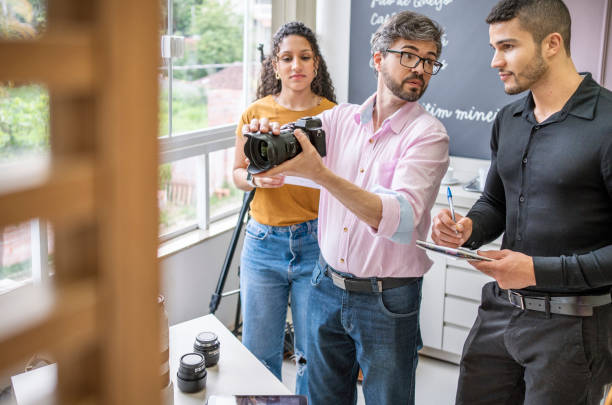 Photographer teaching two students about camera gear in his studio