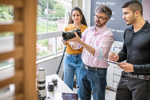 Two young assistants taking notes while learning about camera gear from a professional photographer during a class in his studio