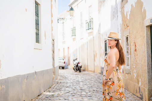 Portrait of an attractive tourist woman in old town Wearing stylish long dress, bracelets and straw hat.