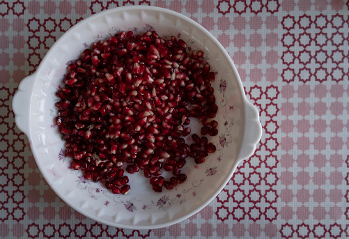 Bowl filled with pomegranate seeds and pomegranate fruit on a table. Selective focus.