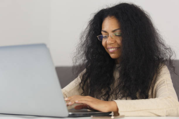 istock Happy black woman in glasses working on notebook computer with a smile. Cheerful BIPOC female in 30s typing text on laptop at home 1462049621