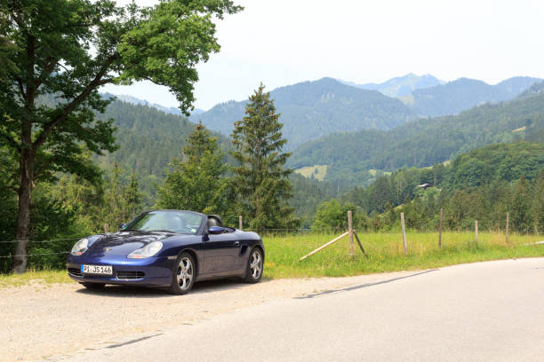 bayrischzell, niemcy - 24 lipca 2021 r.: niebieski roadster porsche boxster 986 z panoramą alp bawarskich na german alpine road. samochód to dwumiejscowy samochód sportowy z silnikiem umieszczonym centralnie produkowany przez porsche. - germany landscape nissan roadster zdjęcia i obrazy z banku zdjęć