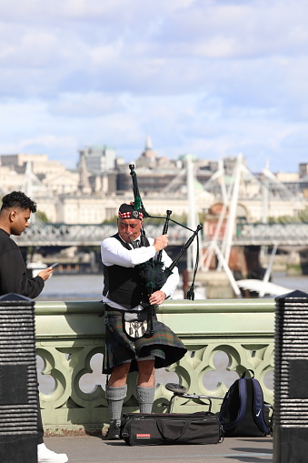 London, United Kingdom - September 18 2022: Scottish bagpiper playing the bagpipes to entertain tourists and Londoners. Beautiful sunny autumn day in the capital of Great Britain.