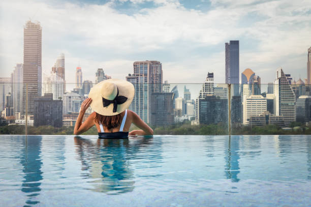 eine frau mit hut genießt den erhöhten blick über die urbane skyline von bangkok - vacations infinity pool relaxation women stock-fotos und bilder