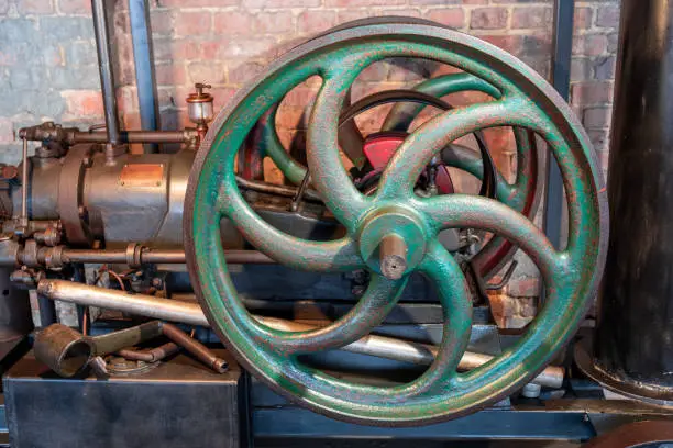 Small steam engine. Green metal flywheel. Industrial exhibition. Red brick wall in the background.