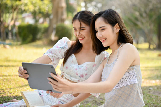 istock Two beautiful young Asian women are using tablet, taking selfies while picnic in the park. 1462059793