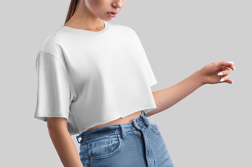 White crop top mockup on posing girl in jeans, isolated on background, front view. Free cut clothing template, empty oversized t-shirt, shirt for design, print, brand, advertising