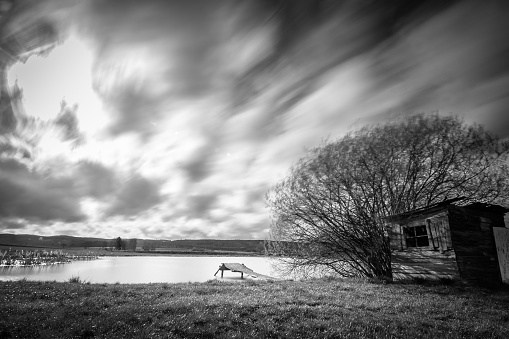 A grayscale long exposure shot of an abandoned wooden house by the lake