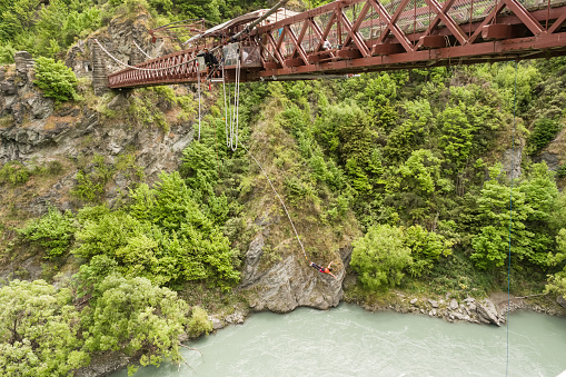 Kawarau Bridge, Queenstown, New Zealand - 20th December 2022: A bungy jumper hangs above the Kawarau River near Queenstown in New Zealand after jumping from the Kawarau Bridge, the birthplace of bungy jumping