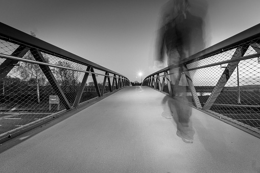 A grayscale shot of a pedestrian walking on the brigde above the street