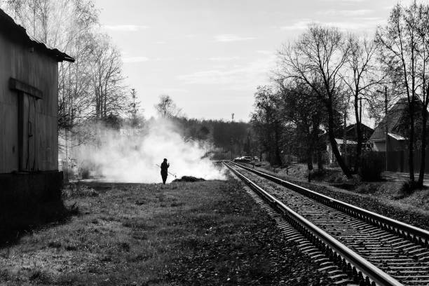A grayscale shot of a man burns leaves in the fall