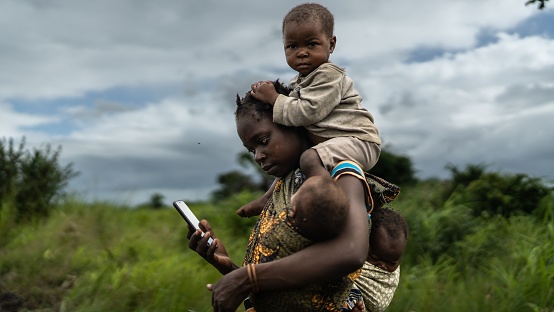 Beira, Mozambique – March 21, 2022: A mother carrying her three children with a smartphone in her hands in Beira, Mozambique