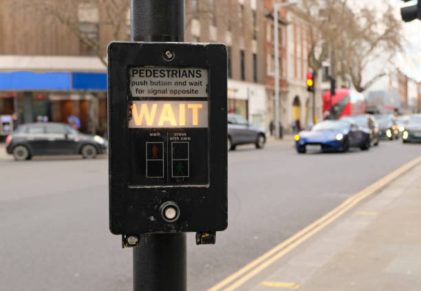 istock Crosswalk button for pedestrian with light warning WAIT in London, UK. Defocused background with Cars drive along road and bokeh from headlights. Button for pedestrians. 1462083118