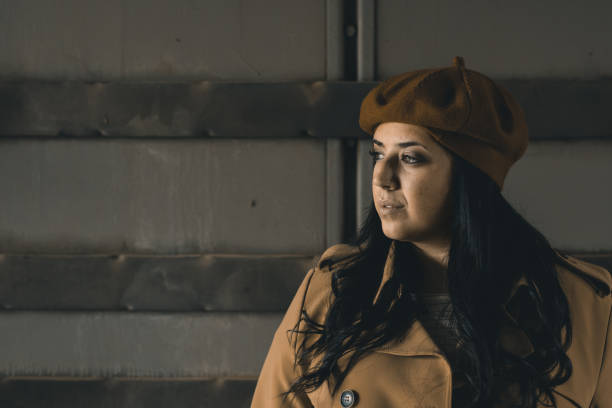 A cheerful young woman with long blonde hair wearing a red beanie and green shirt frames her portrait with a wooden frame against a purple background, conveying fun fashion and creative casual lifestyle.