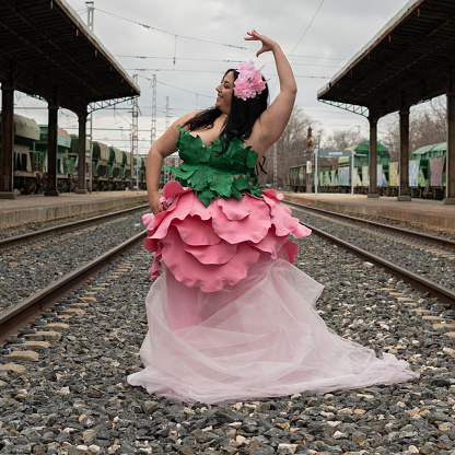Fat woman in a flower dress on an abandoned train track. Flower costume. Train station and flower costume.