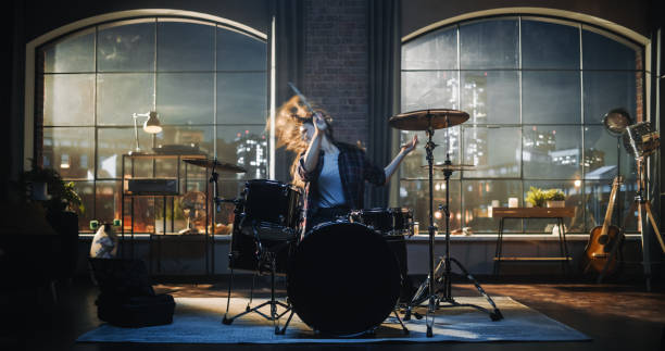 istock Beautiful Young Drummer Playing at a Band Rehearsal, Doing Tricks with Drumsticks. Learning Drum Solo on Drums and Cymbals in Evening Living Room Loft Apartment. 1462107293
