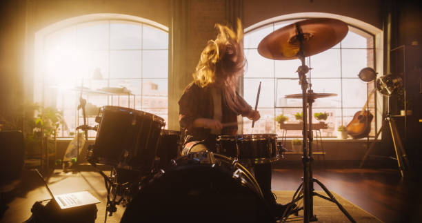 istock Beautiful Young Drummer Playing at a Band Rehearsal, Doing Tricks with Drumsticks. Learning Drum Solo on Drums and Cymbals in Sunny Living Room Loft Apartment. Rock Musician Enjoying Rythm. 1462108491