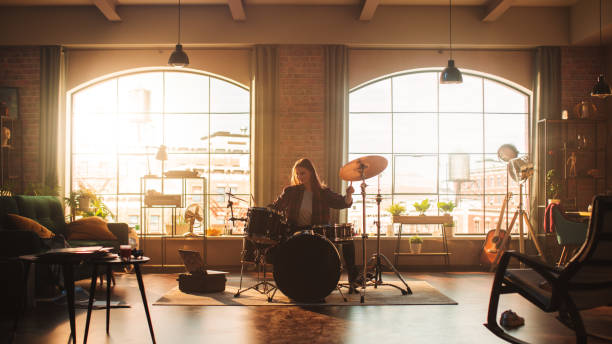 Beautiful Young Drummer Playing at a Band Rehearsal, Doing Tricks with Drumsticks. Learning Drum Solo on Drums and Cymbals in Sunny Living Room of Stylish Loft Apartment.
