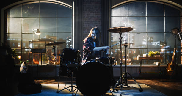 istock Young Female Playing Drums During a Band Rehearsal in a Loft Studio During an Evening or Night Session. Drummer Girl Practising Before a Live Concert on Big Stage with Audience. 1462111885