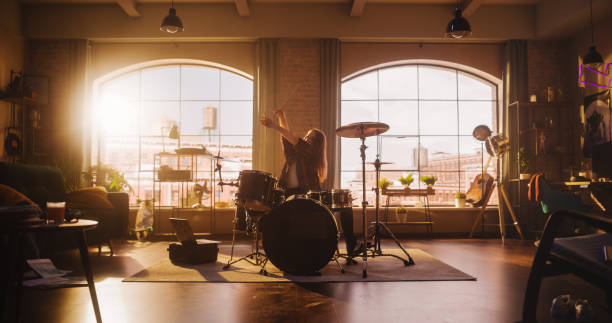 istock Young Female Playing Drums During a Band Rehearsal in a Loft Studio with Warm Sunlight at Daytime. Drummer Girl Practising Before a Live Concert infront of Big Audience. 1462111904