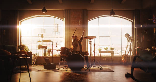 istock Young Female Playing Drums During a Band Rehearsal in a Loft Studio with Warm Sunlight at Daytime. Drummer Girl Practising Before a Live Concert on Stage. Talented Musician Enjoying Music. 1462111990