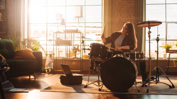 istock Young Female Playing Drums During a Band Rehearsal in a Loft Studio with Warm Sunlight at Daytime. Talented Drummer Girl Practising Before a Live Concert on Stage With Other Musicians. 1462112026