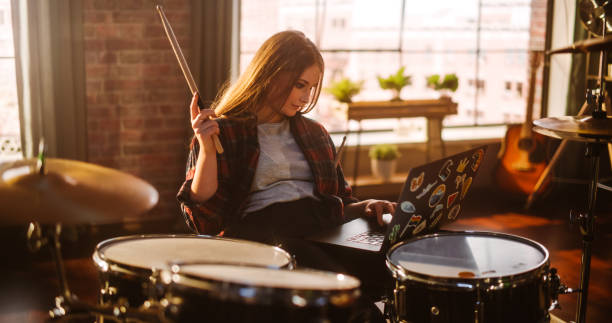 istock Young Musician Taking a Breather, Resting Between Intense Drum Solos. Alternative Stylish Female Using Laptop Computer, Checking Social Media, Chatting with Friends. Loft Living Room on a Sunny Day. 1462112104
