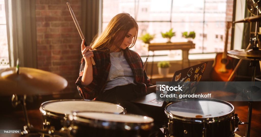 Young Musician Taking a Breather, Resting Between Intense Drum Solos. Alternative Stylish Female Using Laptop Computer, Checking Social Media, Chatting with Friends. Loft Living Room on a Sunny Day. Drummer Stock Photo