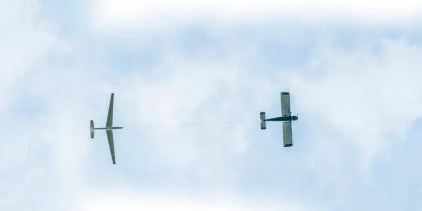 Small private propeller airplane pulling glider airplane in the sky