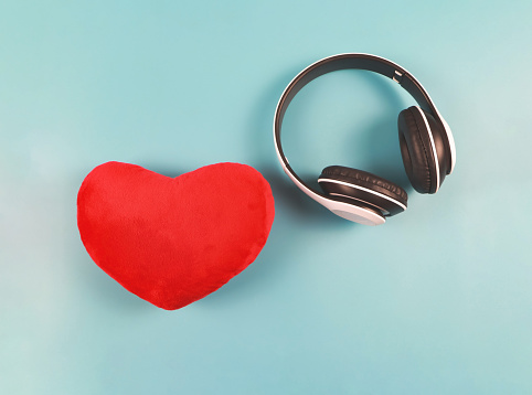 Top view or flat lay o redf heart shape pillow and headdphones on blue background.  Valentine's day,Love songs or podcast concept.