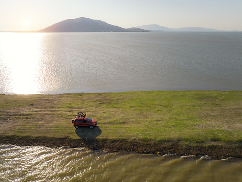 A suv car with a bicycle on the roof is running in a meadow with a lake in the background to find space for camping
