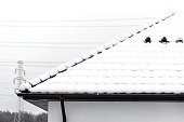 The roof of a single-family house is covered with snow against a cloudy sky, visible ceramic ventilation fireplace on the roof and falling snow.
