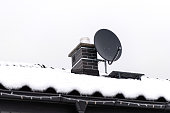 The roof of a single-family house is covered with snow against a cloudy sky, visible ceramic ventilation fireplace and a satellite dish.