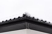 The roof of a single-family house is covered with snow against a cloudy sky, visible ridge tile on the roof and falling snow.
