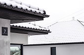 The roof of a single-family house is covered with snow against a cloudy sky, visible ridge tile on the roof and falling snow.