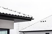 The roof of a single-family house is covered with snow against a cloudy sky, visible ridge tile on the roof and falling snow.