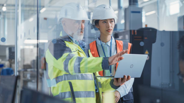 istock Asian Quality Control Specialist Conducting an Industrial Facility Check with the Help of Middle Aged Engineer in a Research and Development Factory. Engineers Shows Work Reports on Laptop Computer. 1462123481