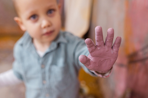 A close-up view of an adorable little boy with blond hair and blue eyes working in his father's workshop. He is learning to paint the wall.