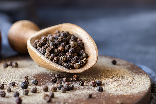 Heap of black pepper, peppercorns in spoon with milled powder on rustic background, dried spice peppercorn concept