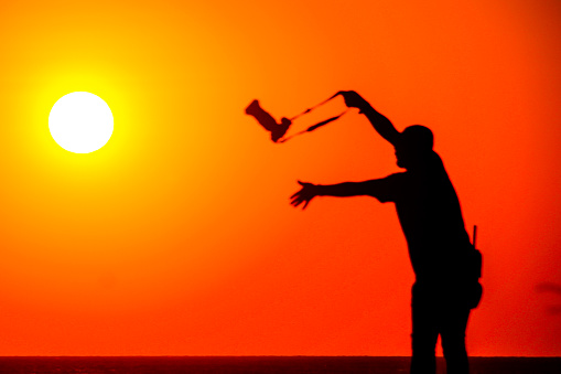 Sportsman with golf swing standing at course against sky. Male golfer is practicing at sunset. He is swinging club.