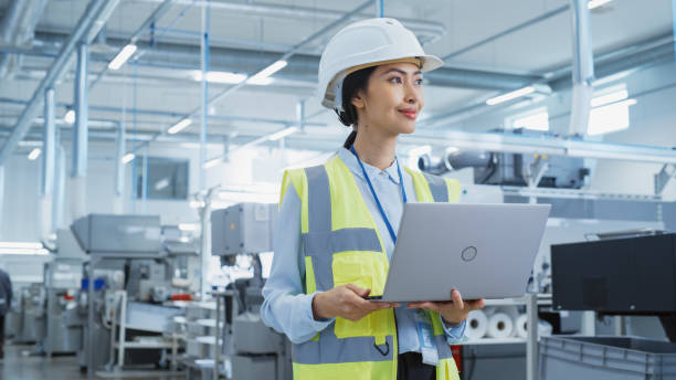 istock A Happy and Smiling Asian Female Engineer in White Hard Hat Standing with Laptop Computer at Electronic Manufacturing Factory. Successful Employee Focusing on PC Screen 1462146312