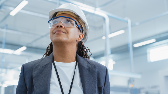 Close Up Portrait of a Happy and Smiling Middle Aged African Female Engineer in White Hard Hat Standing at Electronics Manufacturing Factory. Black Heavy Industry Specialist Posing for Camera.
