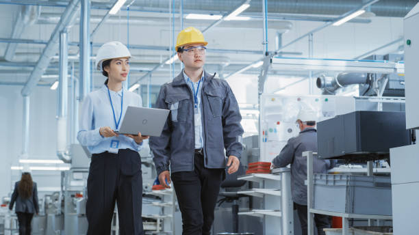 istock Two Young Asian Heavy Industry Engineers in Hard Hats Walking with Laptop Computer and Discussing Work Process in a Factory. Two Manufacturing Employees at Work in Production Facility. 1462149067