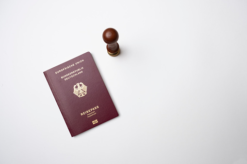 Gronau, NRW, Germany, 01.12.2023: a german passport on a white background and a stamp standing next to it. Schengen visa. Obtaining a visa and a visa abroad. Germany visa. Close-up from the top.