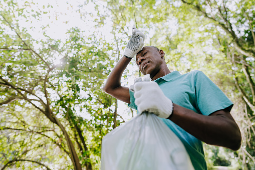 Exhausted man picking up garbage in nature