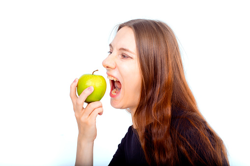 Pregnant woman propose apple for her belly copy space. Beautiful expectant lady having fresh snack, gray studio background. Healthy nutrition and pregnancy concept