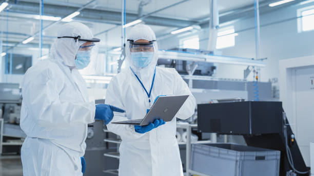istock Two Engineers in Sterile Coveralls Standing in a Heavy Industry Factory, Using Laptop Computer, Examining Industrial Manufacturing Machine Settings and Configuring Production Functionality. 1462155706