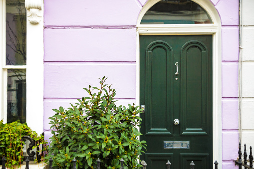 The colorful pastel facade and forest green front door of a traditional terraced London mews townhouse.