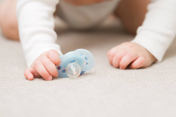 Baby boy crawling on carpet and holding light blue soother with hand. Front view. Closeup.